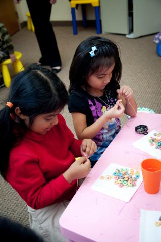 101413clues069.jpg Two young girls putting beads on thread