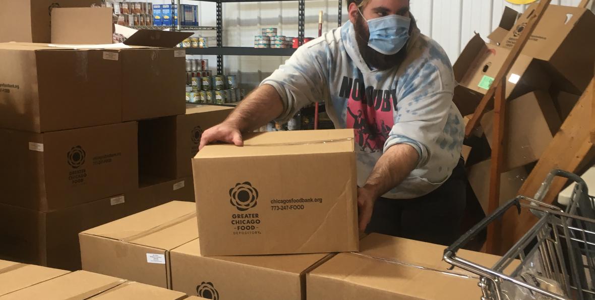blue_cap_food_pantry.jpg A male wearing protective face mask lifts boxes in pantry warehouse setting