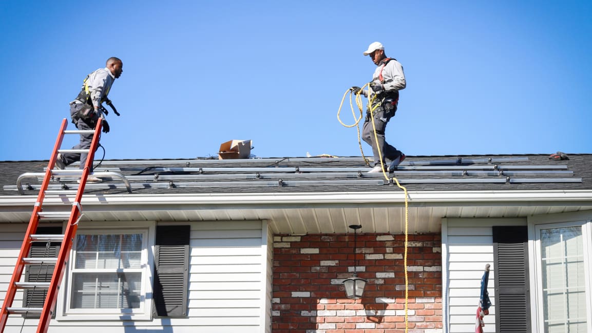 Two men work to install solar on the top of a one-story home.