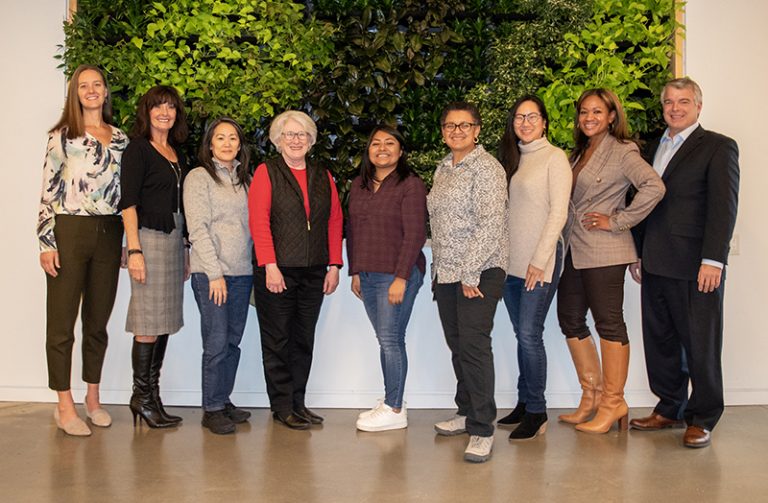 A group photo of nine people of the Kresge Environment Program team standing in front of a green plant “living wall.”