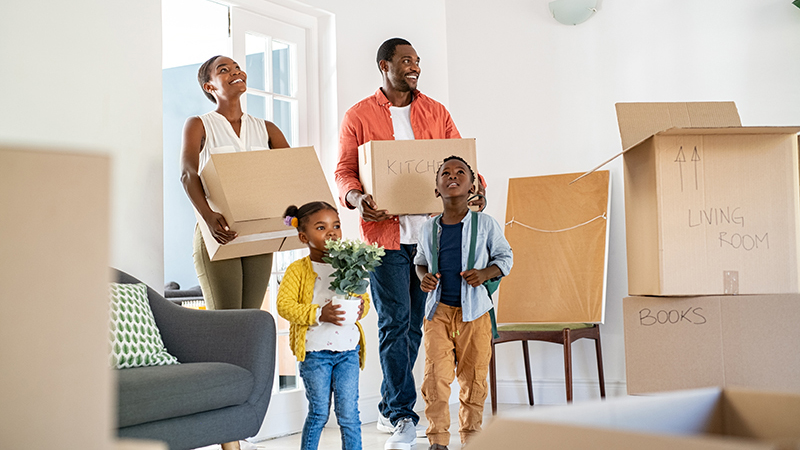 Beautiful African American family with two children carrying boxes in a new home. Cheerful mother and father holding boxes while entering new home with happy son and daughter helping parents relocating in new house.