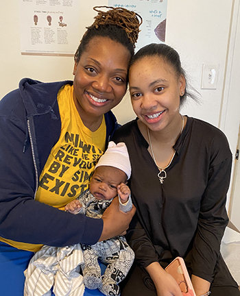 Two woman sitting close together holding a baby. 
