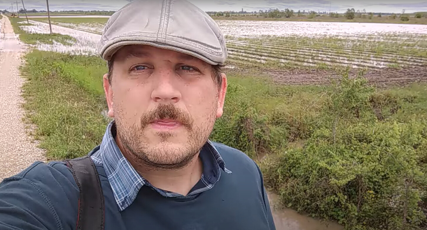 A man with a hat is standing in front of a large agricultural field
