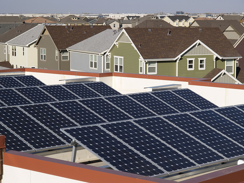 A row of solar panels is seen in the foreground and a row houses in the background.