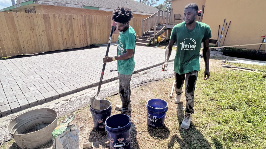 Two workers with green Thrive New Orleans T-shirts are working in the back yard of a home.