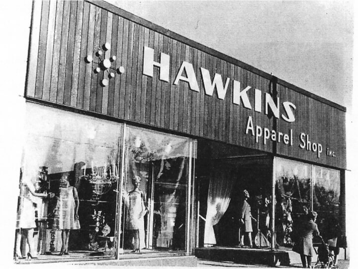 Photo of storefront with high-fashion clad mannequins in the window. Sign says HAWKINS Apparel Shop inc.