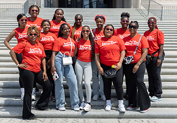 A large group of girls and women all in orange shirts that say "Youth Day at the Capitol" are standing on the steps of the Capitol. 