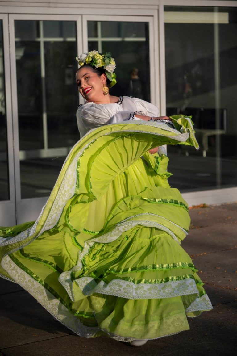 A performance by the Milagro Compañía de Ballet Folklórico with a woman in a colorful lime color dress and flowered headdress.