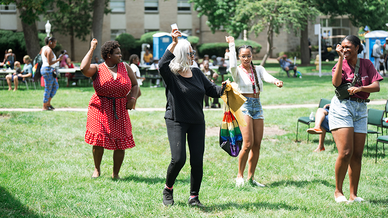 A group of women are doing a line dance in a field at a block party. 