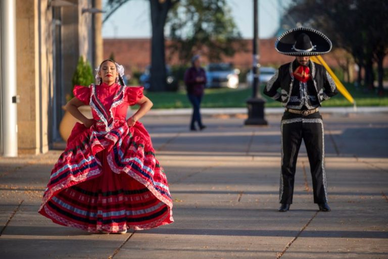 A performance by the Milagro Compañía de Ballet Folklórico with a woman in a colorful red Mexican style folklorico dress with flowing skirt and a man in a black sombrero, jacket and pants trimmed in white.