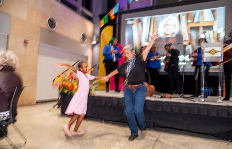 A woman and a child dance as a mariachi band plays behind them.