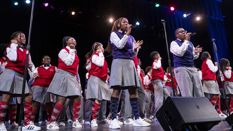 The Detroit Youth Choir in red or blue vests and white shirts sing on stage.