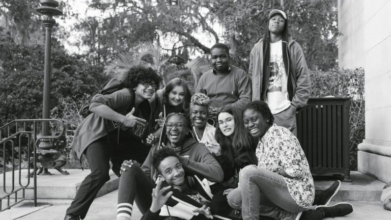 A black and white image shows a group of teens and young adults playfully posing for a photo.