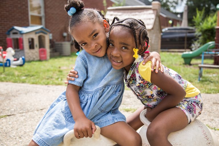 Two little girls hug outdoors at a childcare center.