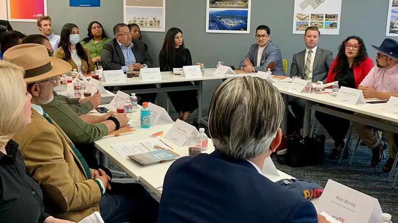 A group of people are seated at tables shaped in a square for a meeting.