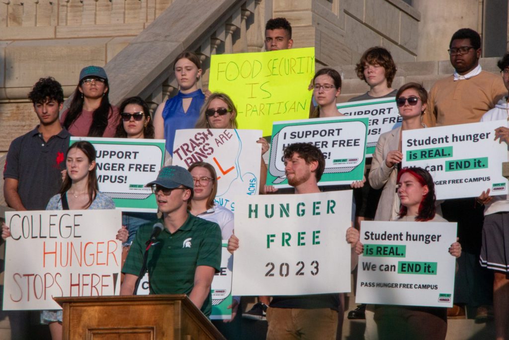 A group of students holding signs like Hunger Free 2023 and College Hunger Stops Here stand on the. steps of a capitol building.