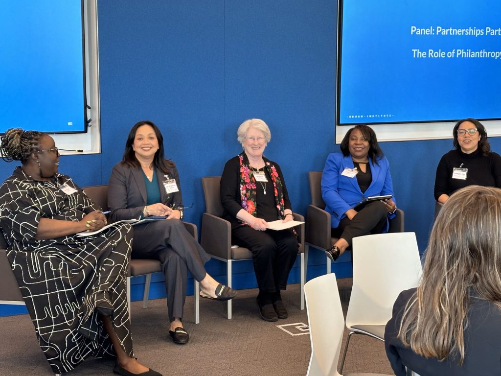 Five women are seated on a stage for a panel discussion on The Role of Philanthropy