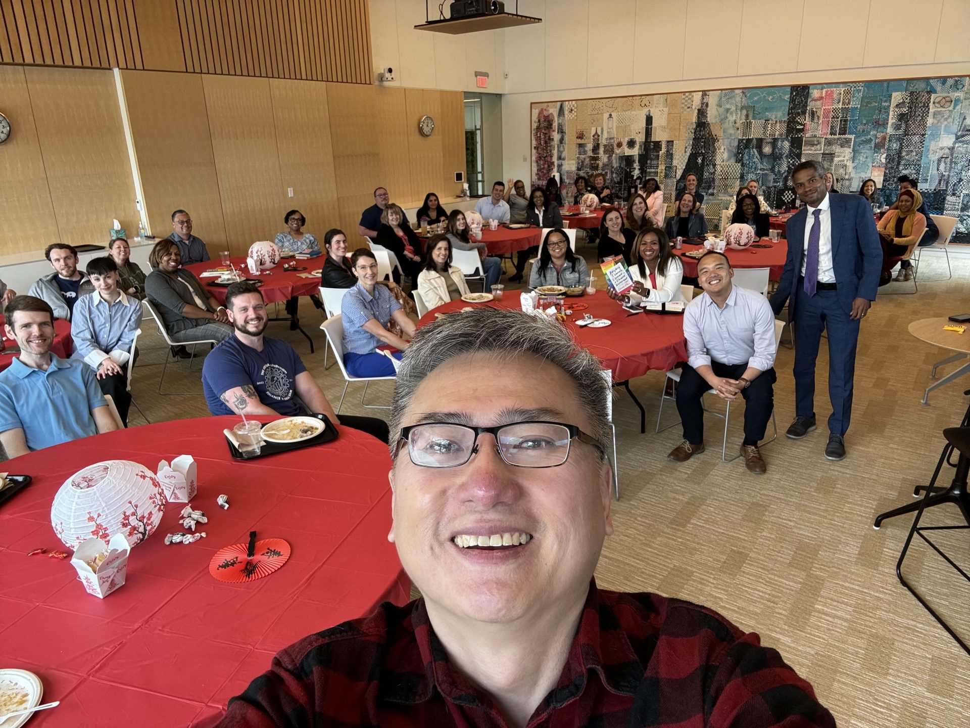 Curtis Chin, a Chinese-American author, takes a selfie with a room full of Kresge staff behind him.