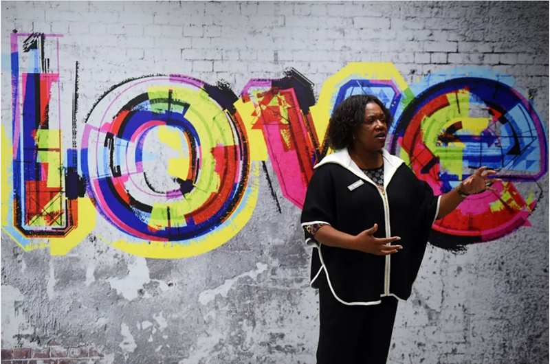 Incubate Neighborhood Center Founder Canieria Gardner stands in front of a wall with a mural wit the word love spelled out in a mixture of colors.