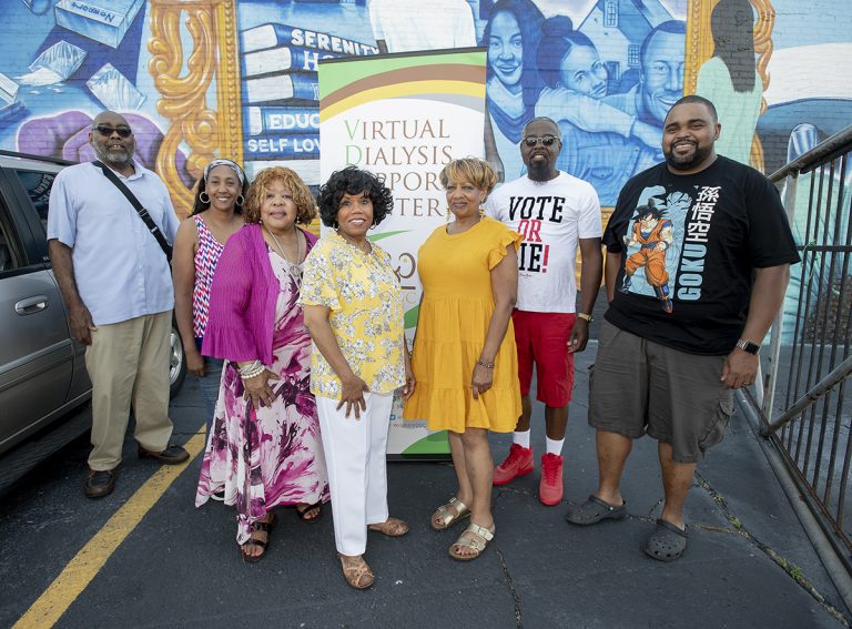 Group of seven adults posed in what appears to be a parking lot in front of pop-up banner that says Virtual Dialysis Support Center