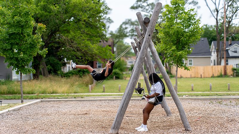 Two kids swinging on a swing set in a park in northwest Detroit.