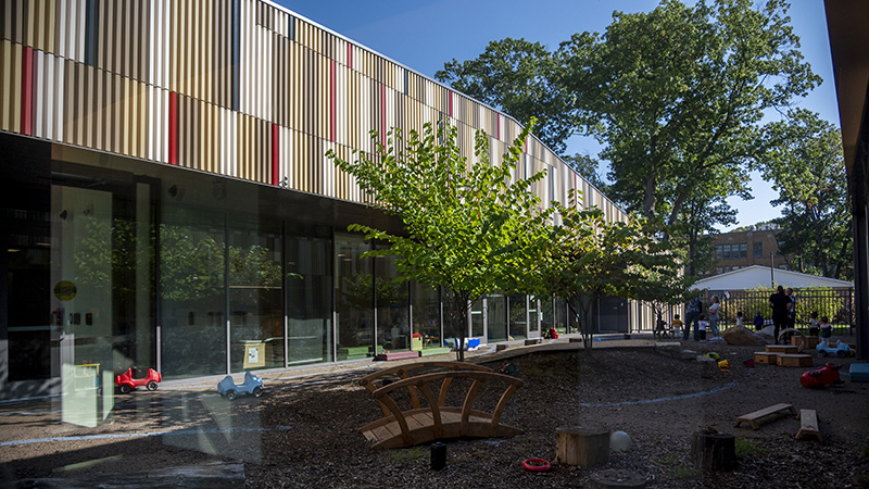 A multi-colored terra cotta roofline with a building containing tall windows and an outdoor courtyard with a children's playground. 