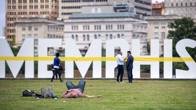 People are enjoying a park that includes large block letters that spell Memphis. The Memphis skyline is seen in the background.