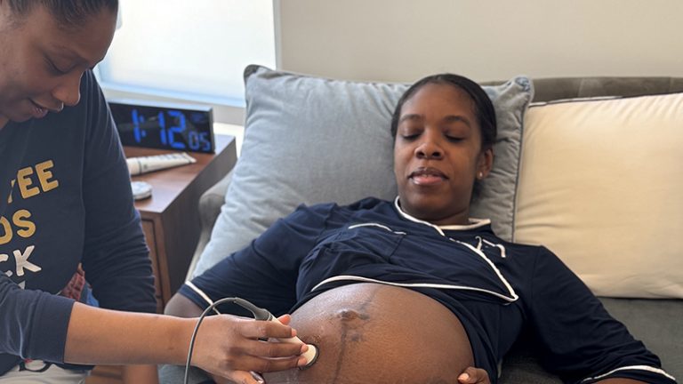 A midwife is holding a stethoscope to a pregnant woman's belly.