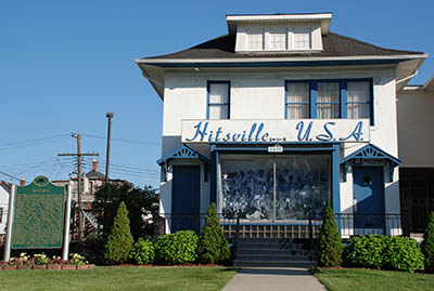 A white house with blue trim and the sign Hitsville USA above the proch. 