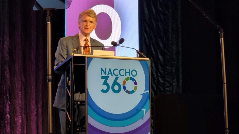 Kresge President Rip Rapson is standing on a stage behind a podium with the NACCHO 360 logo.