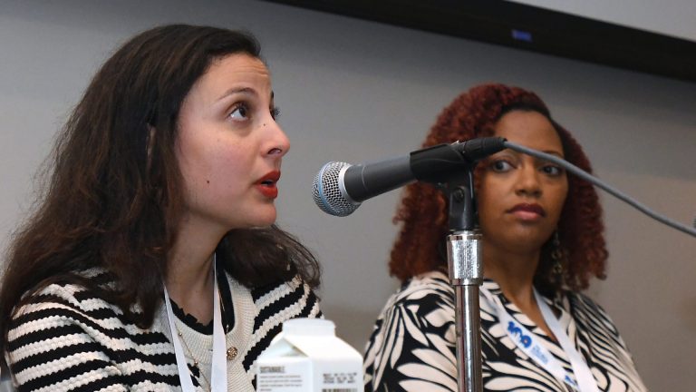 Two women speakers at a convening panel sit at a table with microphones.