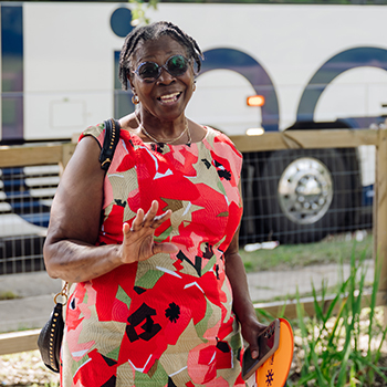 A Black woman in a colorful dress of res, beige, white and black patterns. 