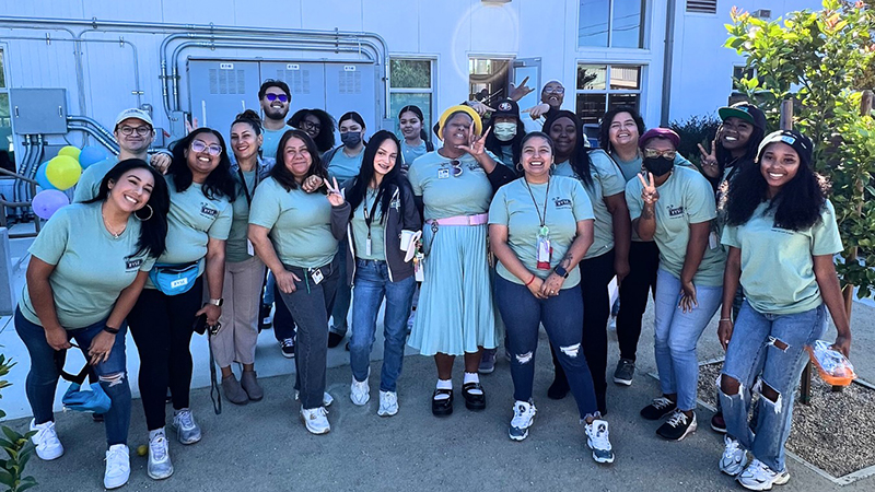 A large group of young people pose for a photo in front of a building with blue walls.
