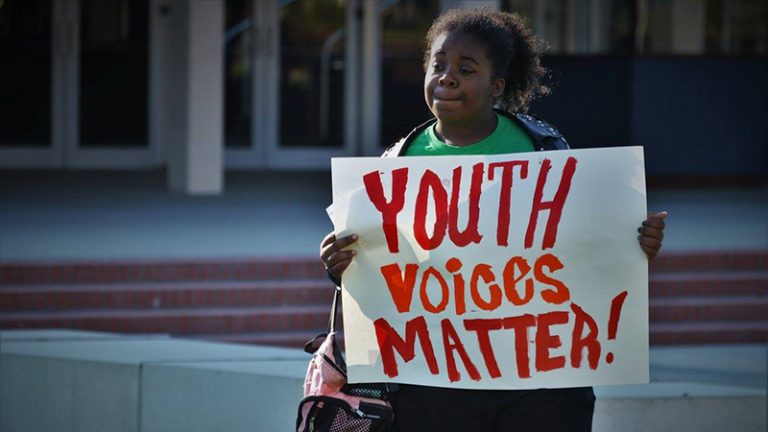 A Black woman holds up a sign that says Youth Voices Matter!