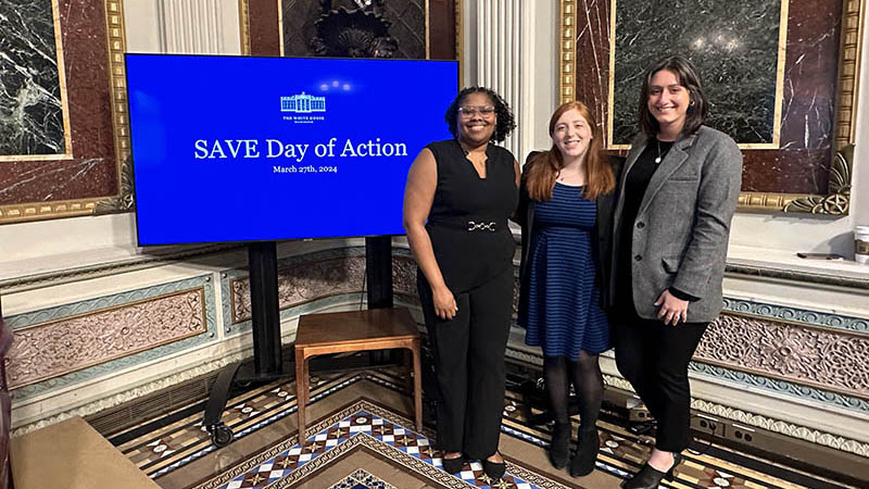 Three people from Civic Nation pose next to a screen with the words: SAVE Day of Action March 27, 2024