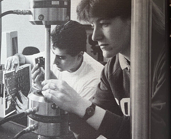 Two students are working with scientific equipment in a lab.
