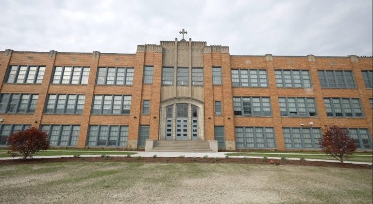 1940s style school with orange brick and possibly concrete or grey stone facade, arched door, crucifix on top