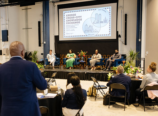 A man with a microphone asks a question to the four panelists sitting on a stage.