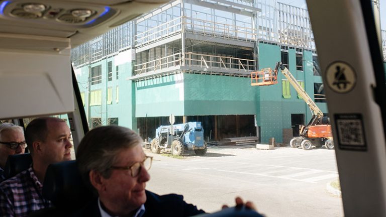 People on a bus tour look out the window at a construction site.