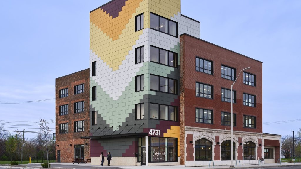 The LOVE Building is seen from a street corner. A five-story brick building with a colorful corner segment.