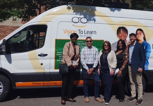 Five people stand on the side of a white mobile clininc van with a Vision to Learn logo. 