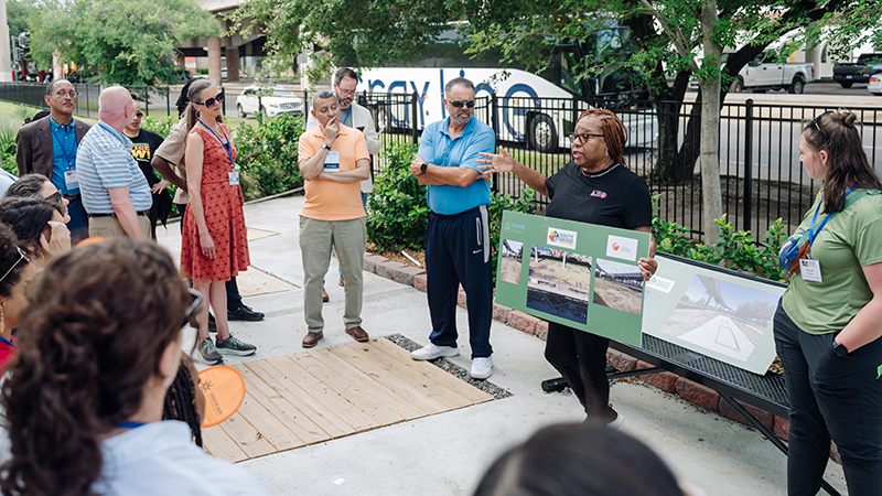 A woman is holding a poster board and talking to group of people at a stormwater management park. 