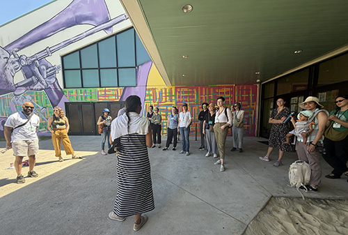 A group of people gather in a courtyard in front of a mural of a Musician playing a trombone.