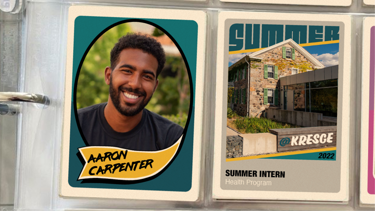 A binder with two vintage-style baseball cards in plastic inserts. The first card on the left features a photo of a male student intern and his name: Aaron Carpenter. The second card features a photo of a brick farmhouse and a connecting modern building with windows and the text: @Kresge 2022 | Summer Intern | Health Program