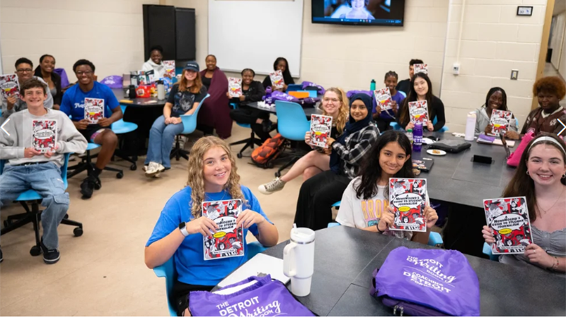 A large group of young students are seated in a classroom holding up books.