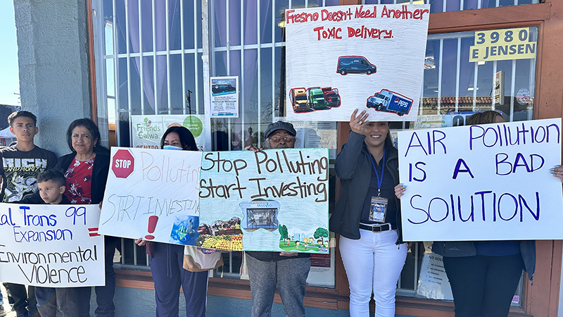 A group of people standing in front of a building are holding up signs that oppose a harmful project proposed in their neighborhood.