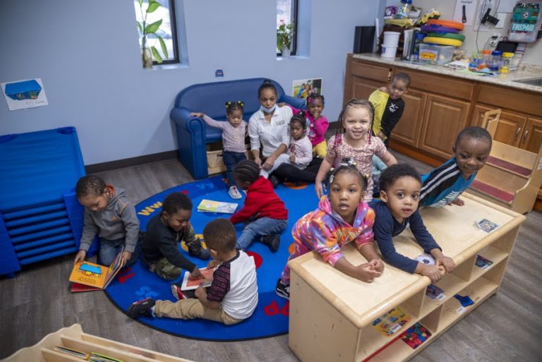 A group of young children and a child care professional are seen playing.