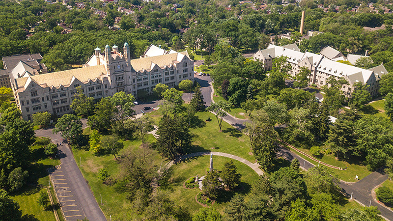 An aerial view of the 53-acre Marygrove College campus focused on two historic Tudor Gothic structures and a large open green space in front of the buildings.
