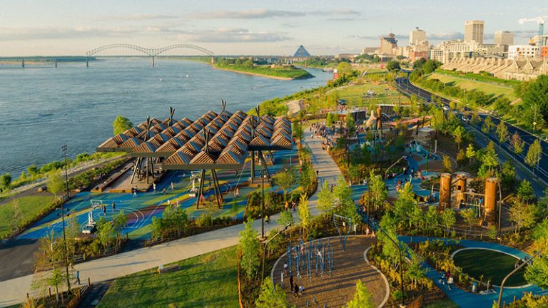 An aerial view of the renovated Tom Lee Park with playgrounds, trails, covered spaces on the riverfront with a skyline view of downtown Memphis in the background