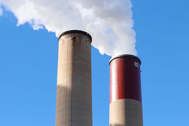 A photo of the top of two smoke-emitting power plant smokestacks.